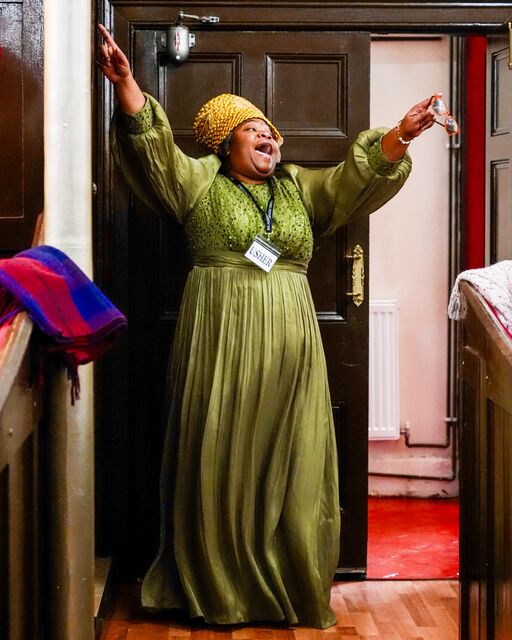 Woman in a green dress standing with both arms raised beside the church doorway.