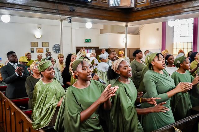 Congregation standing together, with women in green in the foreground.