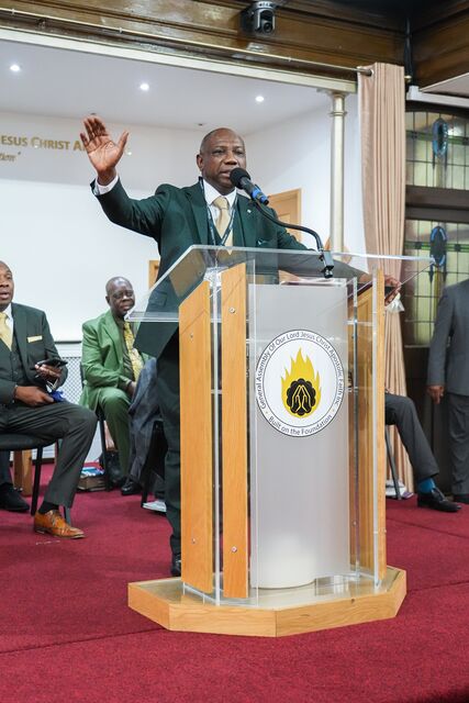 Man at the church lectern raising one hand as he addresses the congregation.