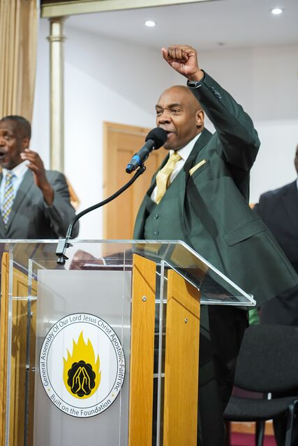 Man in a dark green suit speaking at the lectern with one arm raised.