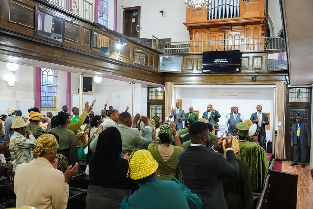 Wide view of the congregation standing beneath the church balcony.