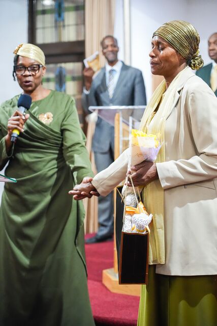 Woman in a cream jacket and patterned headwrap standing beside other attendees.