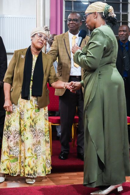 Woman in green speaking into a microphone beside two attendees at the front of the church.