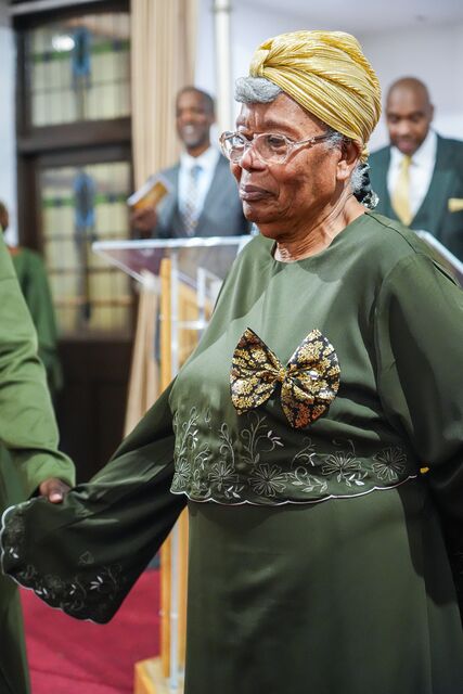 Woman in a green outfit and patterned headwrap standing inside the church.