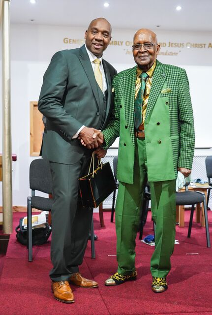 Two men posing together in dark green and bright green suits.