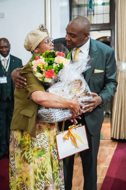 Man standing beside a woman holding a large wrapped bouquet and gift.