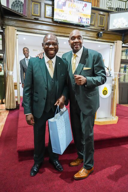 Two men in suits posing together at the front of the church.