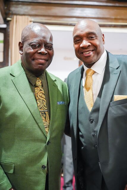 Two smiling men posing together, one wearing a green shirt and the other a yellow tie.