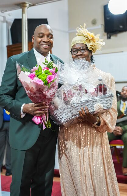 Man holding pink flowers beside a woman in a gold hat holding a wrapped gift.