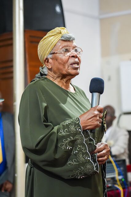 Woman in a green outfit and gold headwrap holding a microphone.