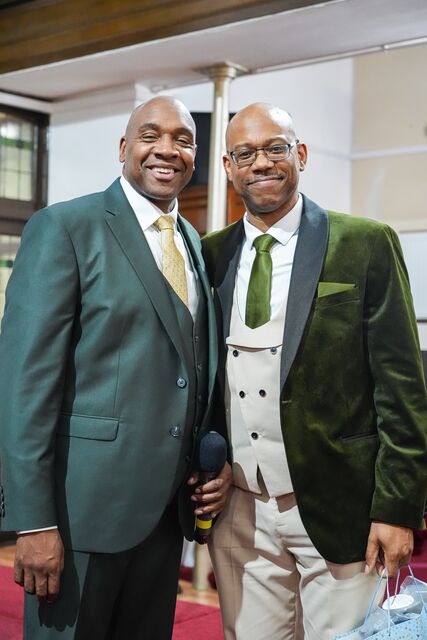 Two men in dark suits posing together inside the church.